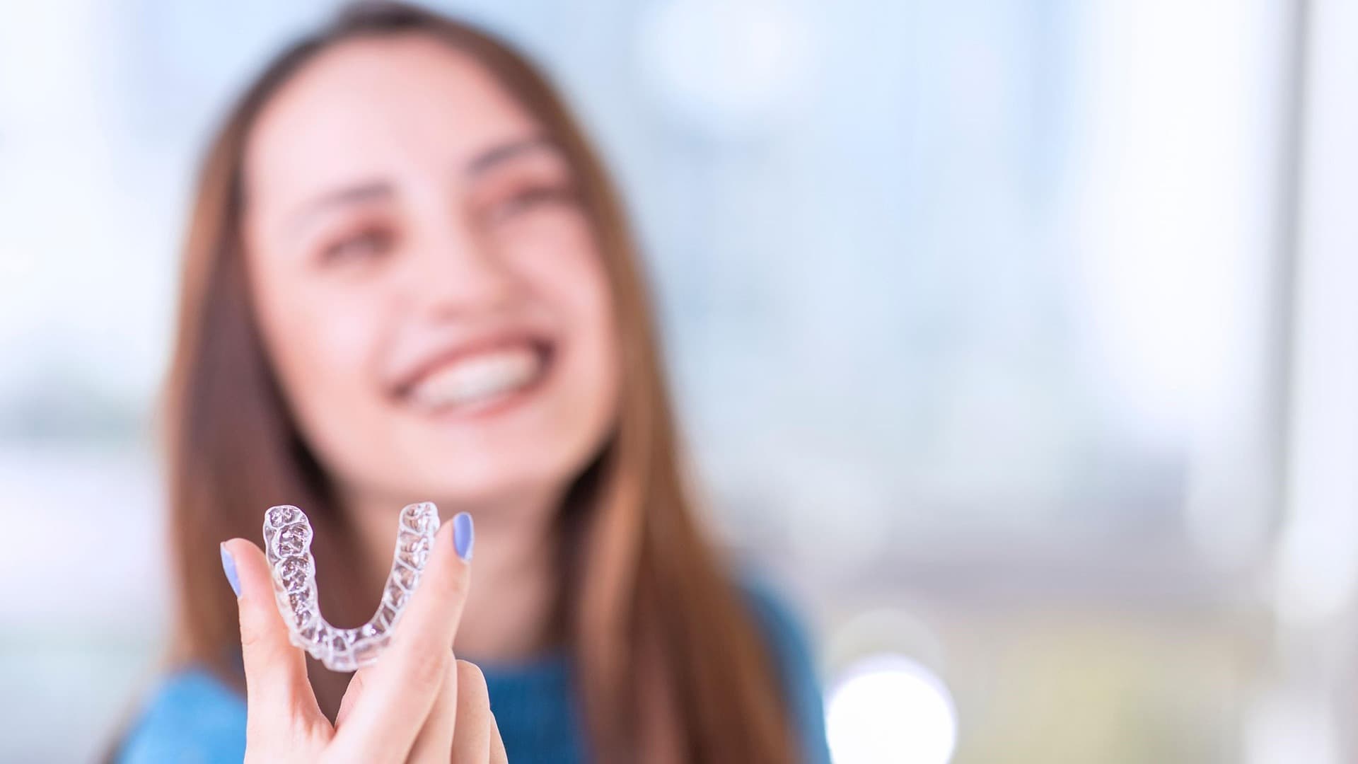 Smiling woman holding a clear Invisalign aligner